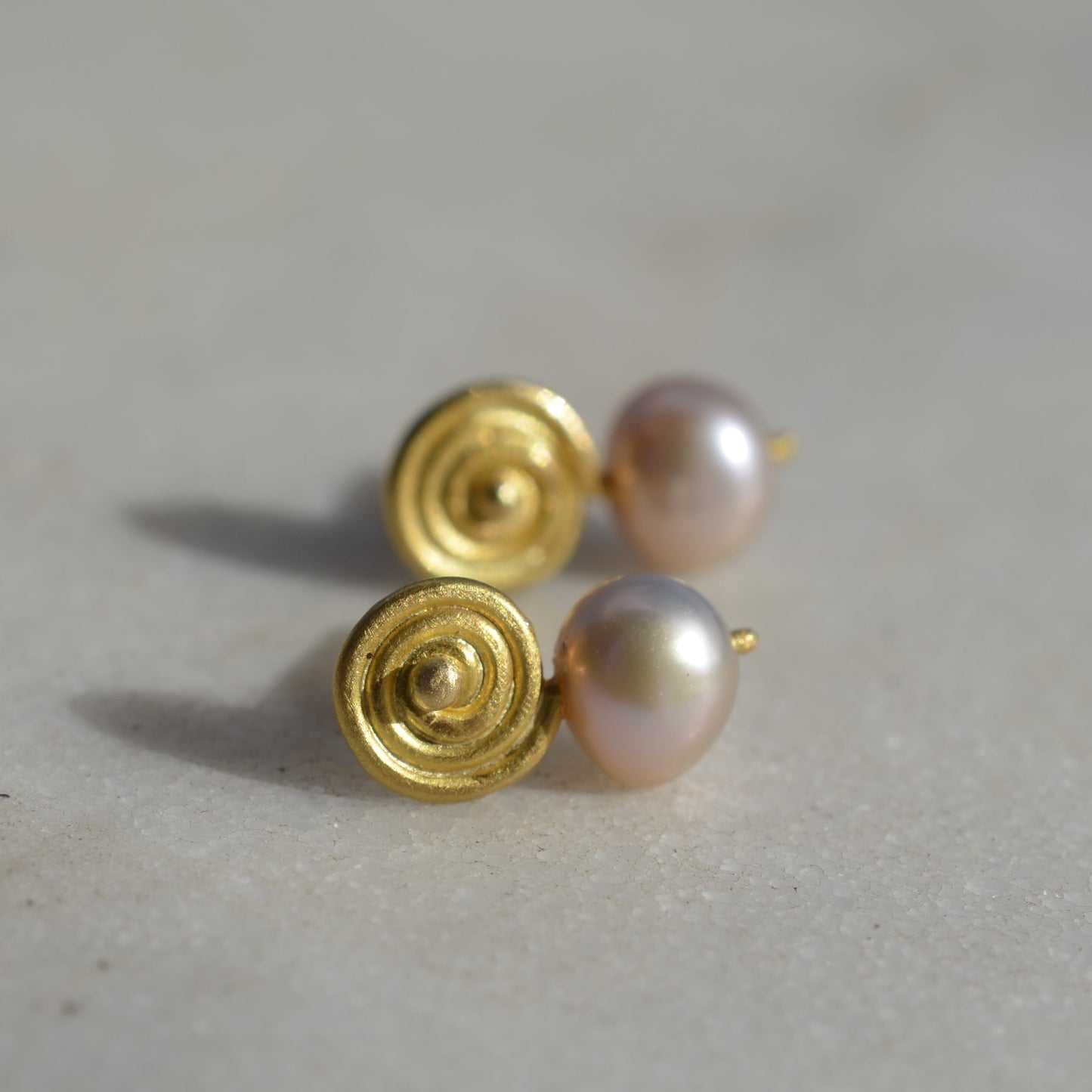 Gold earrings with pink pearls on marble in the sun