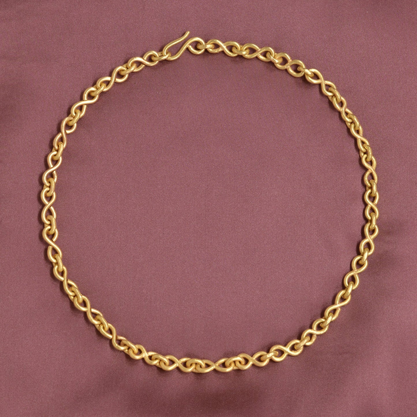 Gold chain necklace on a maroon fabric background
