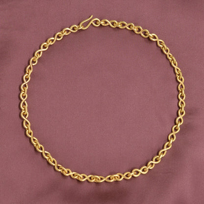 Gold chain necklace on a maroon fabric background