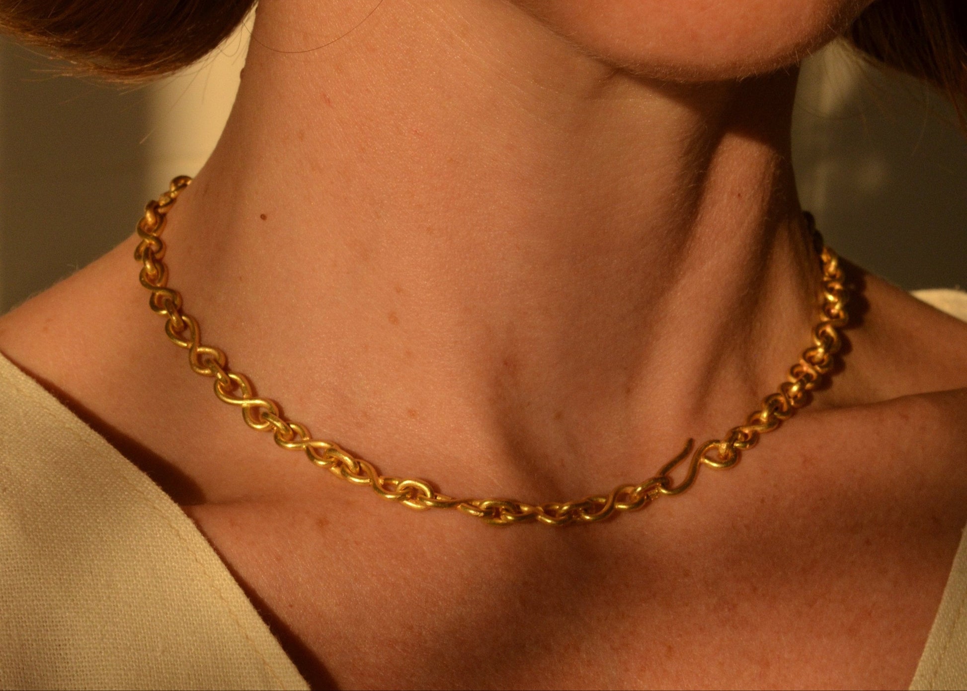 Gold chain necklace on a person's neck with a neutral background