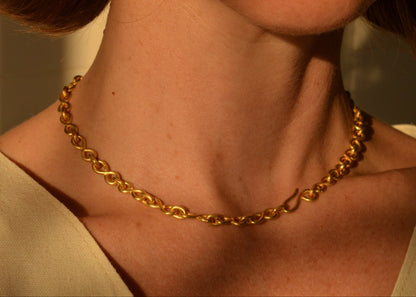 Gold chain necklace on a person's neck with a neutral background