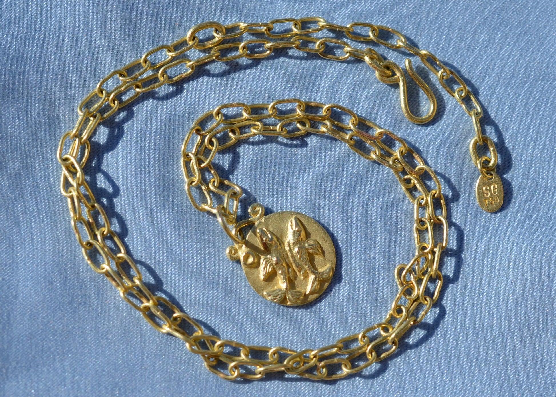 Pisces zodiac pendant on a handmade chain necklace on blue fabric