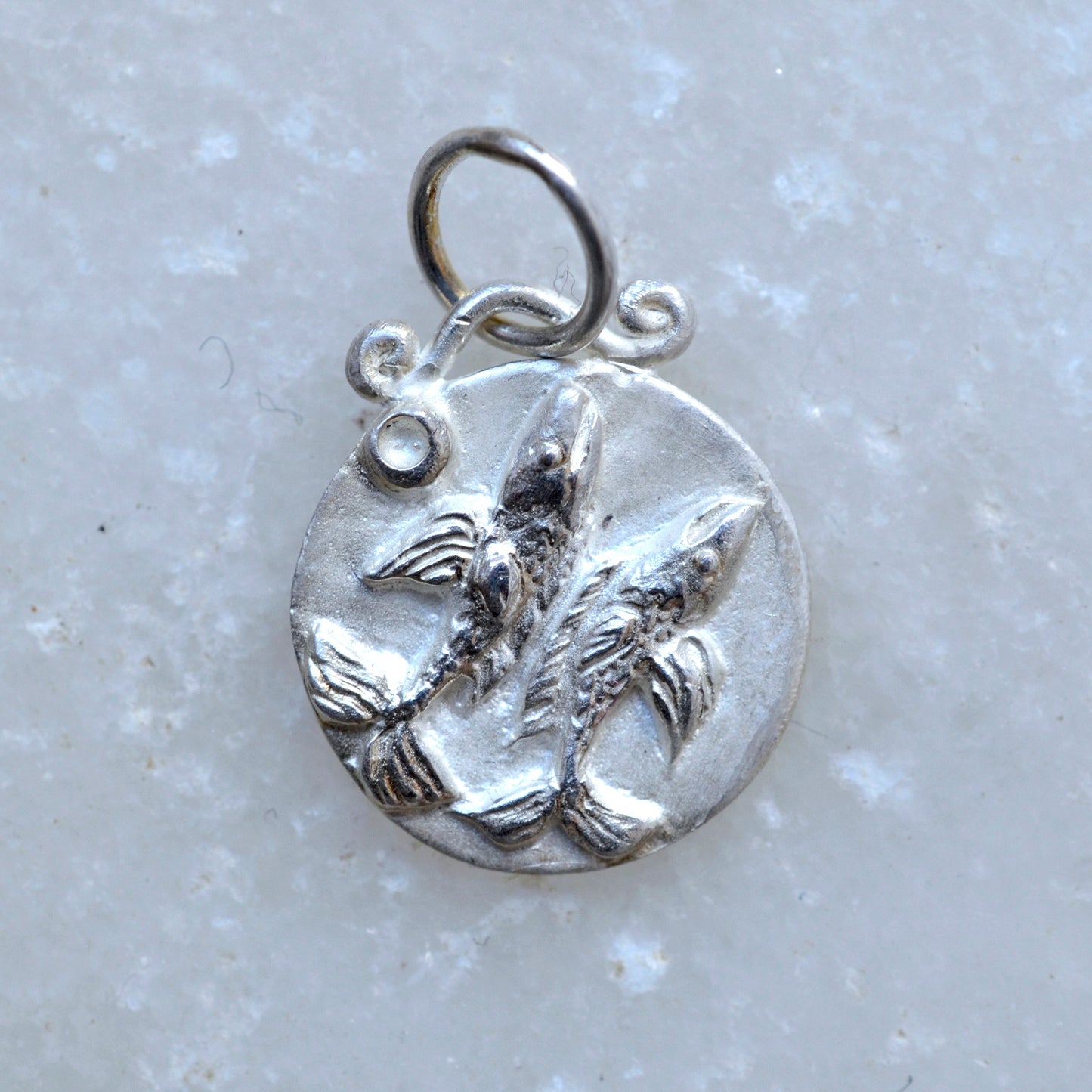 Pisces zodiac pendant in silver on marble