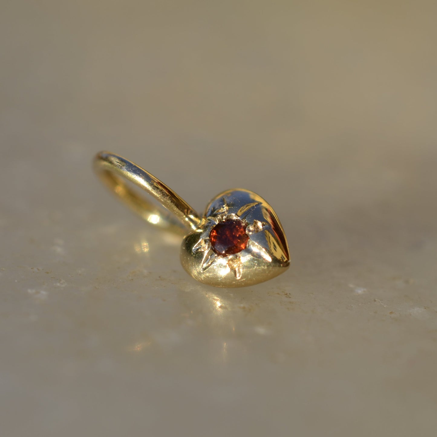 heart shaped gold pendant with a garnet on marble