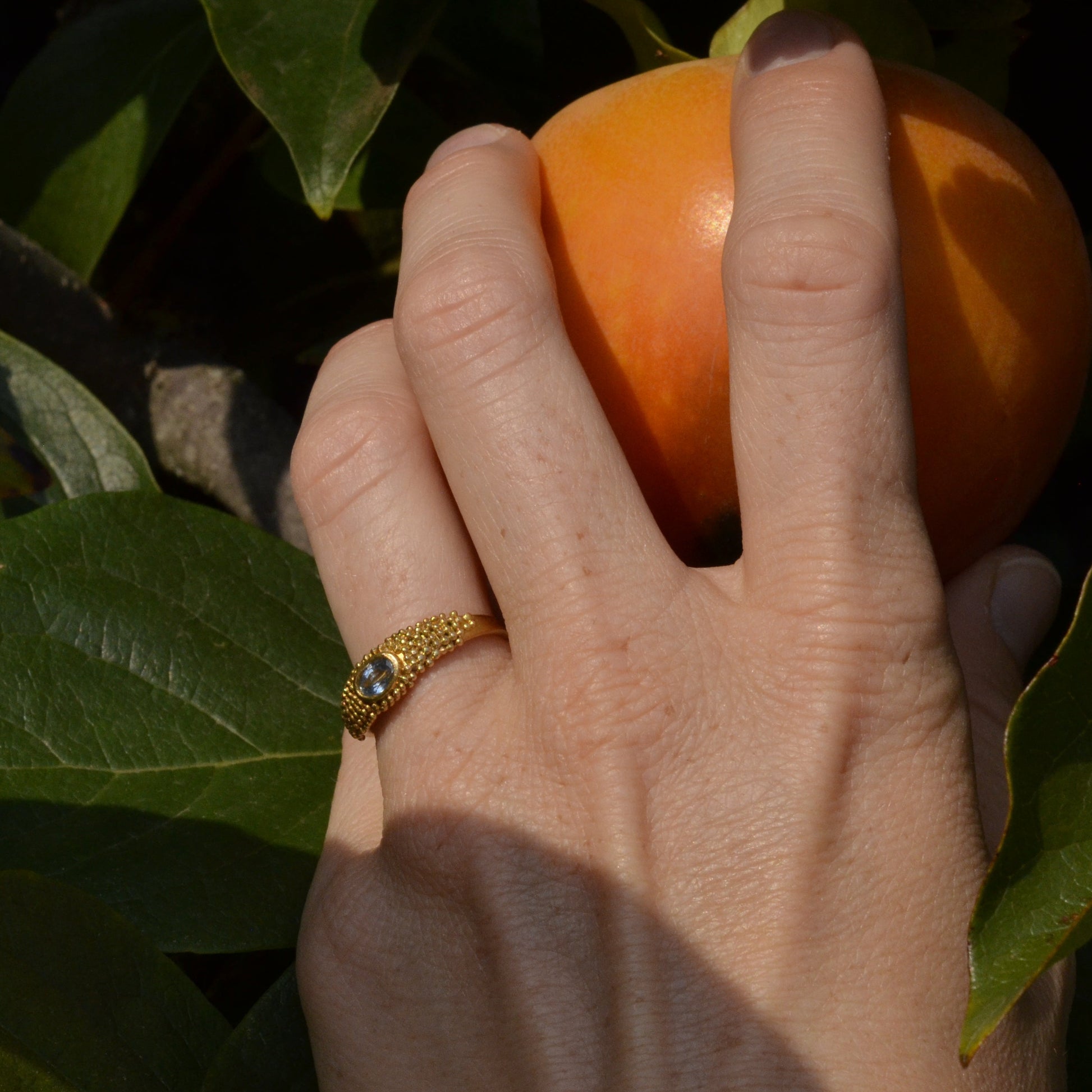 granulated gold ring with blue topaz on a hand picking a fruit