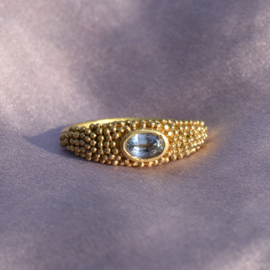 Granulated gold ring with a blue topaz on violet silk