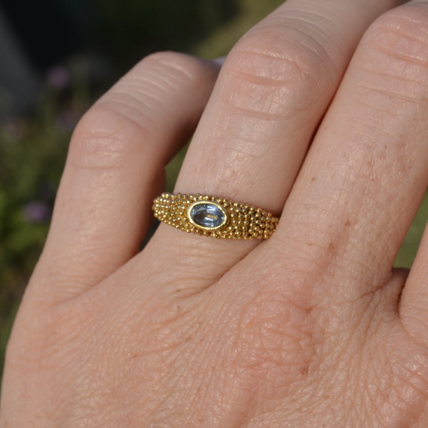 a granulated gold ring with a blue topaz on a finger