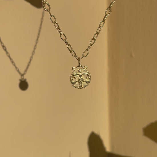 Gold pendant of the zodiac sign libra on handmade paperclip chain dangling in the sun