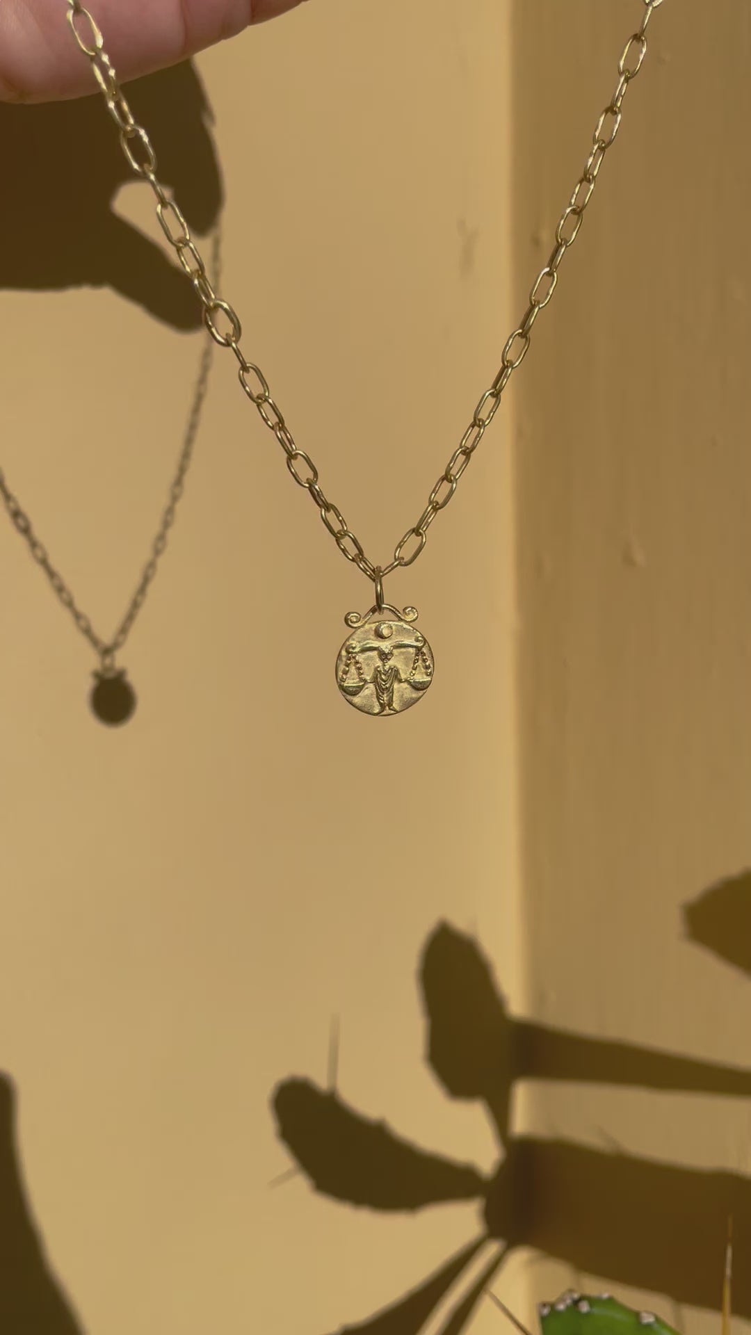 Gold pendant of the zodiac sign libra on handmade paperclip chain dangling in the sun
