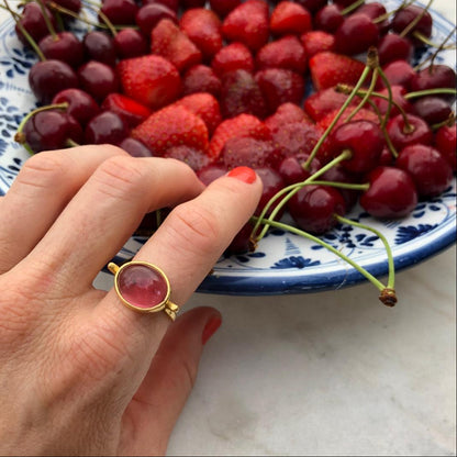 Hand with a gold ring with a pink tourmaline in front of cherries and strawberries on a decorative plate