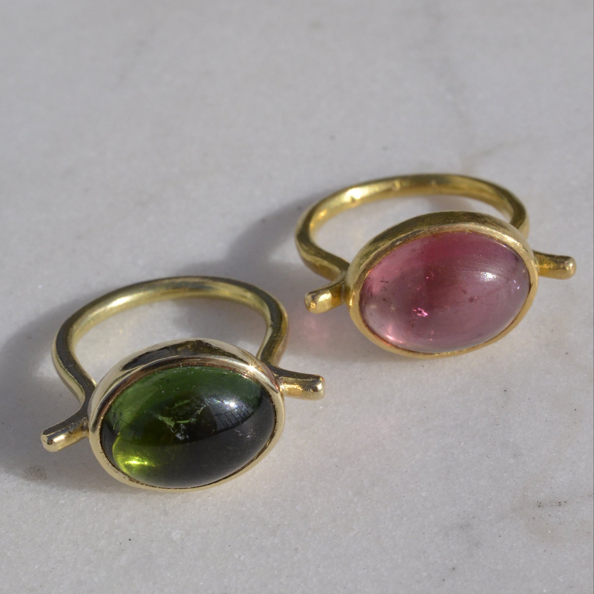 Two gold rings with pink and green cabochon cut tourmalines on marble